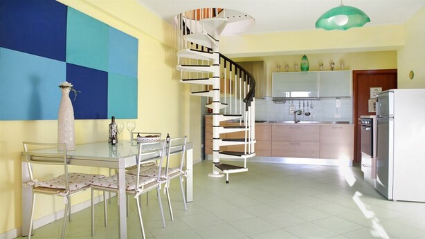 Una cocina moderna con una escalera en espiral, un área de comedor con una mesa de vidrio y una isla de cocina.
