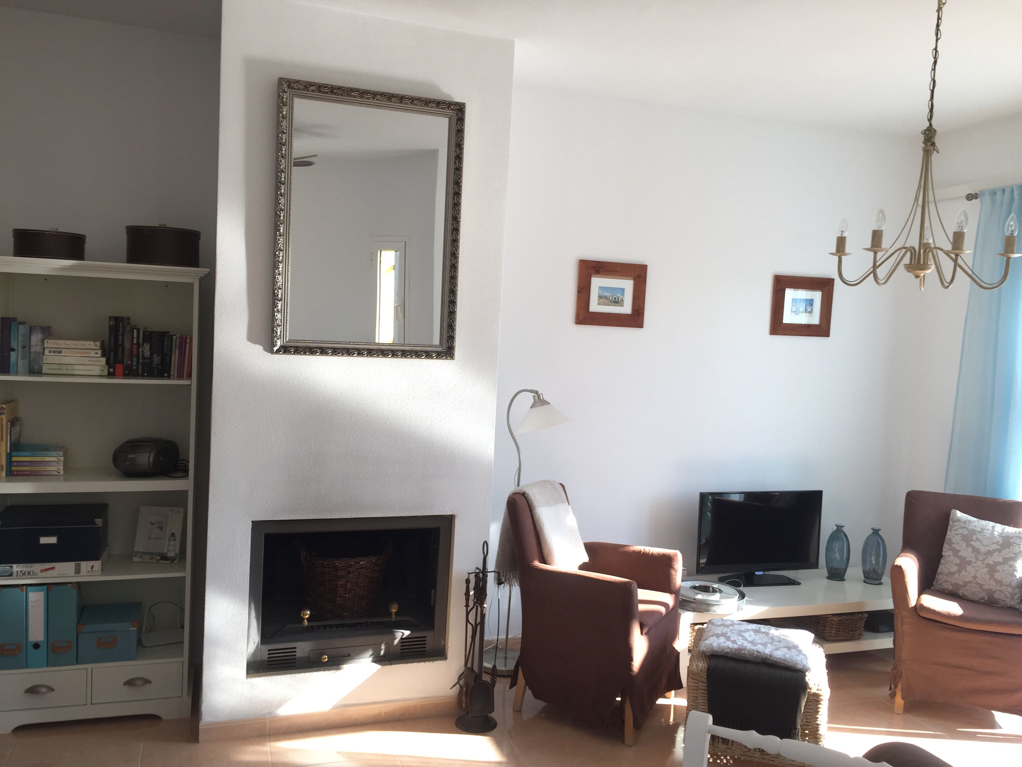 A living room with a fireplace, a television, a bookshelf, and a chandelier.