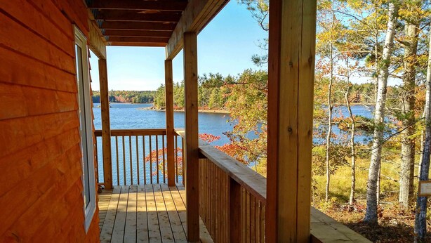 Eine Holzterrasse mit Blick auf einen See und Herbstlaub.