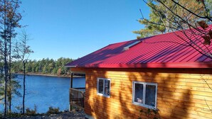 Eine Holzhütte mit rotem Dach, einer Terrasse und Blick auf einen See.