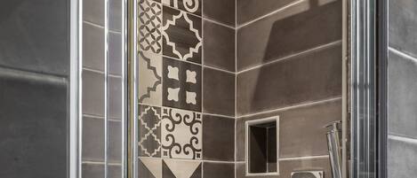Una ducha con puerta de vidrio, azulejos decorados y una ventana pequeña cuadrada.