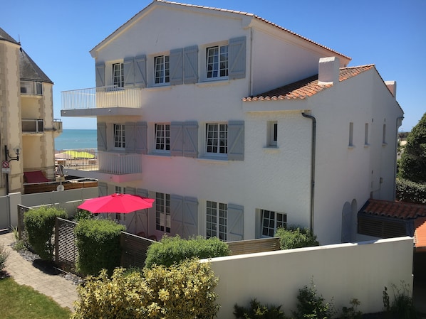 A multi-story building with balconies, a red umbrella, and a view of the sea.
