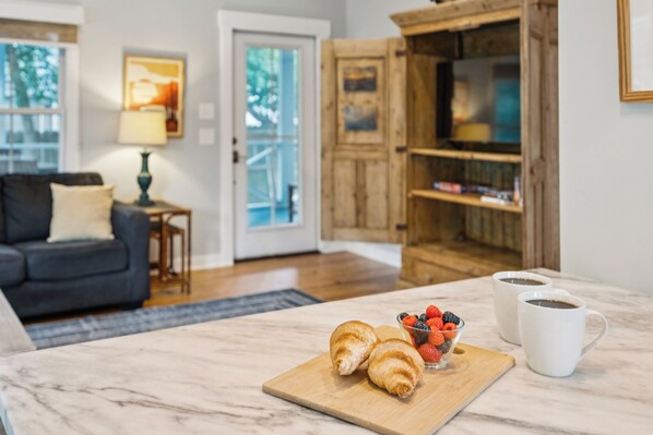 Une cuisine avec un plan de travail en marbre, deux croissants, un bol de fruits rouges variés et deux tasses à café blanches.