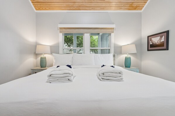 A neatly made bed with two towels, a window with a view of trees, and two lamps on nightstands.