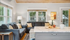 A modern living room with a sofa, a dining table, and a kitchen area. - Stones Throw | Walk to Beach & Center St | 2 Kings + Fenced Yard | Pet Friendly (Folly Beach)