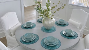 Una mesa redonda para comer con sillas blancas, un jarrón decorativo con ramas y caminos de mesa color turquesa.
