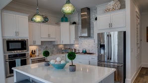 Una cocina moderna con armarios blancos, electrodomésticos de acero inoxidable y una isla central con taburetes.
