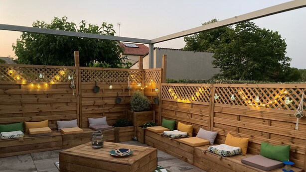 A wooden outdoor seating area with benches and cushions, a central coffee table, and a decorative string of lights. - Villa overlooking the hill between Hyeres and St Tropez (Solliès-Pont)