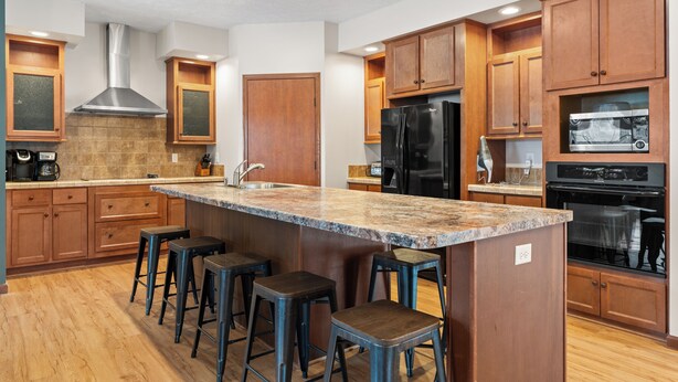 Eine moderne Küche mit Holzschränken, einer Edelstahl-Dunstabzugshaube, einem schwarzen Kühlschrank und einer Granit-Arbeitsplatte.