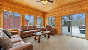 Ein geräumiges Wohnzimmer mit Holzwänden und -decke, großen Fenstern und einem Deckenventilator.