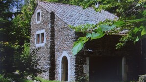 A stone building with a sloped roof, an arched doorway, and a small window. - Les Mazades, gîte  large terrace Labellisé Esprit parc national des Cévennes. (Charnavas)