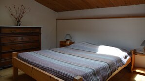 A bedroom with a wooden bed, a dresser, and a nightstand with a lamp. - Les Mazades, gîte  large terrace Labellisé Esprit parc national des Cévennes. (Charnavas)