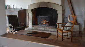 A cozy living room with a stone fireplace, leather armchair, wooden chair, and a coffee table. - Les Mazades, gîte  large terrace Labellisé Esprit parc national des Cévennes. (Charnavas)
