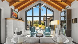 A spacious living area with a high ceiling, large windows, and a view of the outdoors.