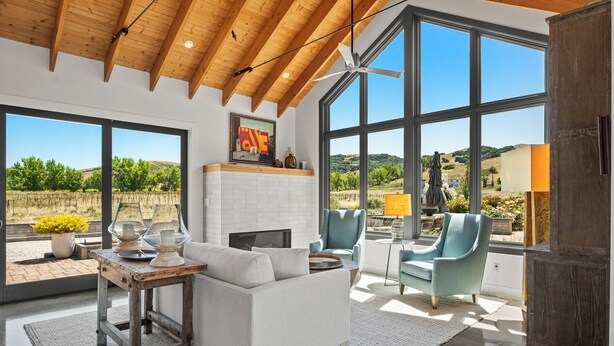 A spacious living room with a fireplace, large windows, and a view of the countryside.