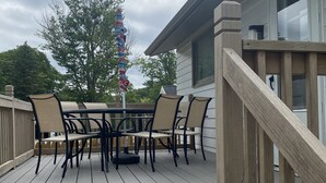 A wooden deck with a table and chairs, a colorful umbrella, and a view of a house in the background.