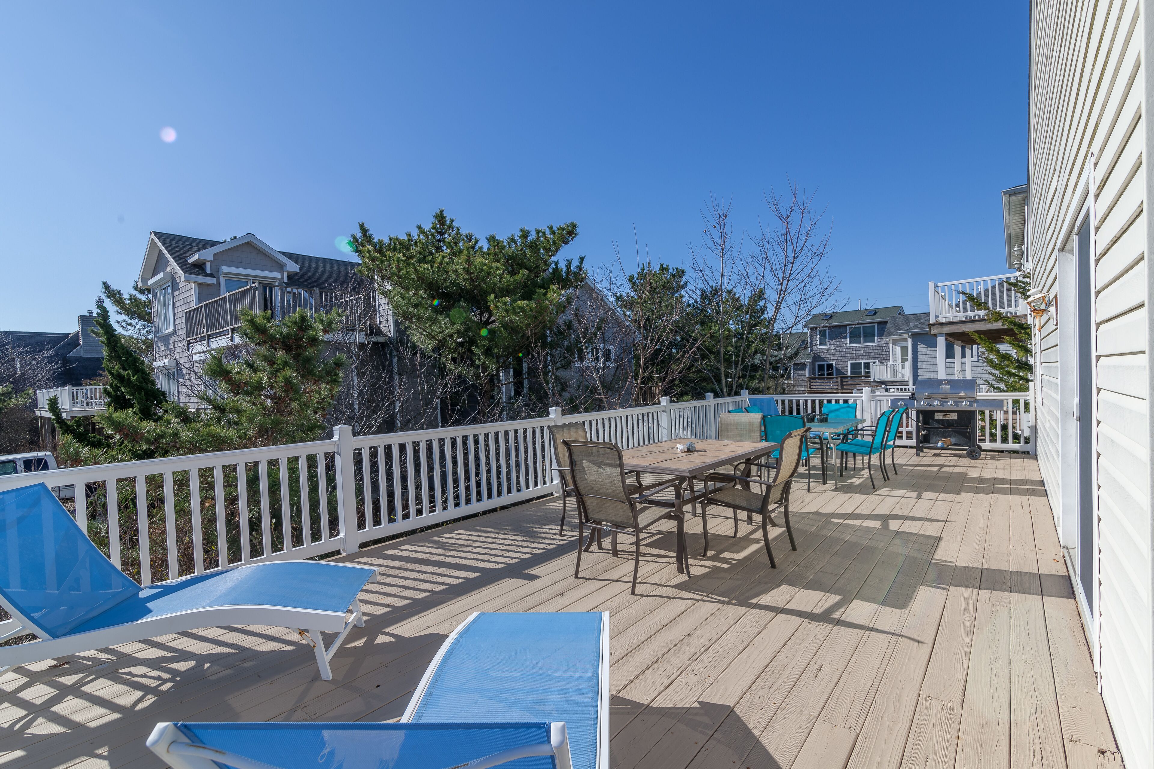 A wooden deck with outdoor furniture, including chairs and a table, surrounded by a white fence.