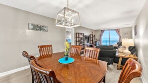 Een eethoek met een houten tafel en stoelen, een hanglamp en uitzicht op de oceaan door een raam.