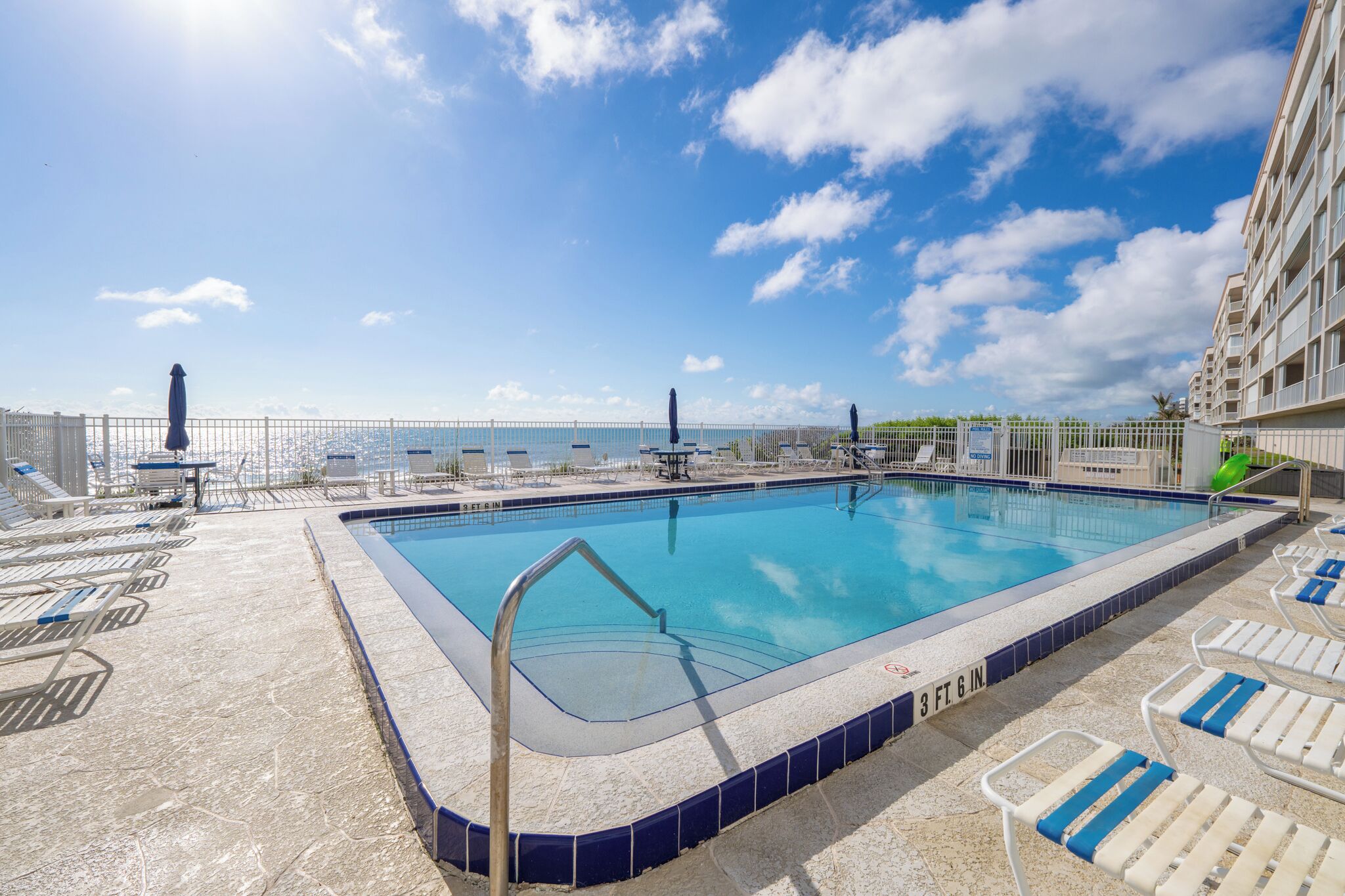 A swimming pool with lounge chairs and a view of the ocean.