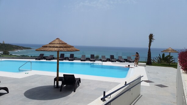Ein Pool mit Liegestühlen und Sonnenschirmen mit Blick auf den Ozean.