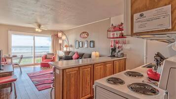 A modern kitchen with wooden cabinets, a central island, and a stove. There is a dining area with a red sofa and a view of the outdoors.