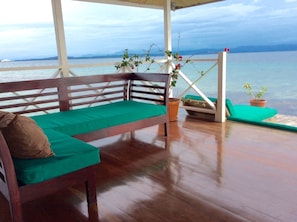 Relax in a serene outdoor seating area with a scenic sea view, featuring a bench and lounge chair with green cushions.