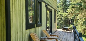 Une terrasse en bois avec deux chaises et une table, donnant sur une zone boisée.