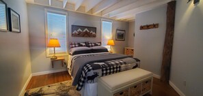 Cozy bedroom with a large bed, two windows, and a wooden bench with storage.