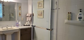 Bathroom features a glass shower enclosure, white sink, and a shelf with toiletries.