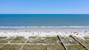 A beach with a wooden boardwalk leading to the water, sandy beach, and umbrellas.