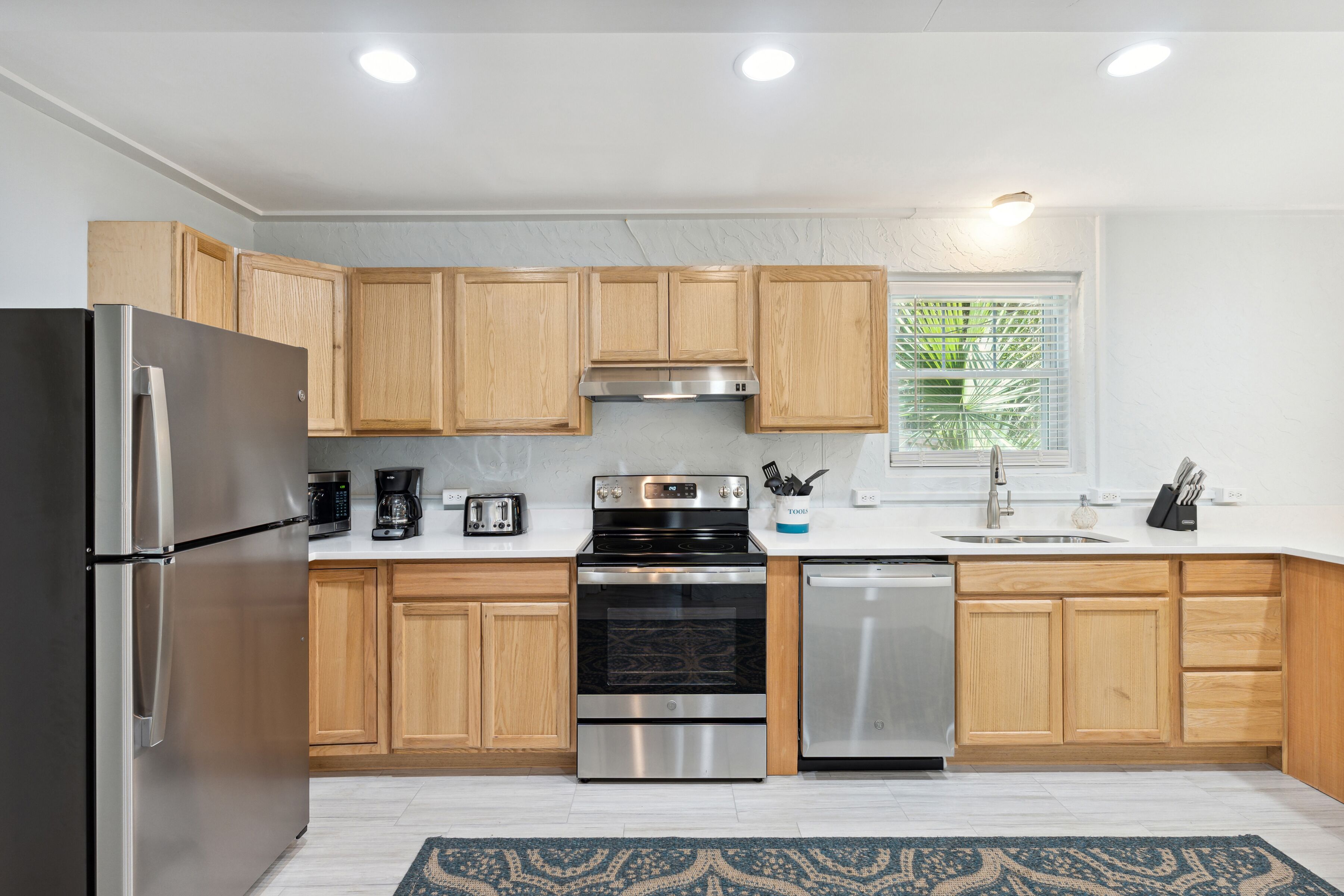 A modern kitchen with wooden cabinets, stainless steel appliances, a coffee maker, and a window with blinds.