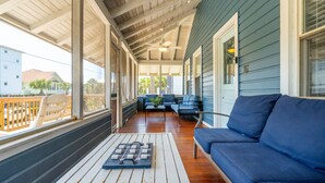 A covered porch with a blue sofa, a wooden table with a board game, and a view of neighboring houses.