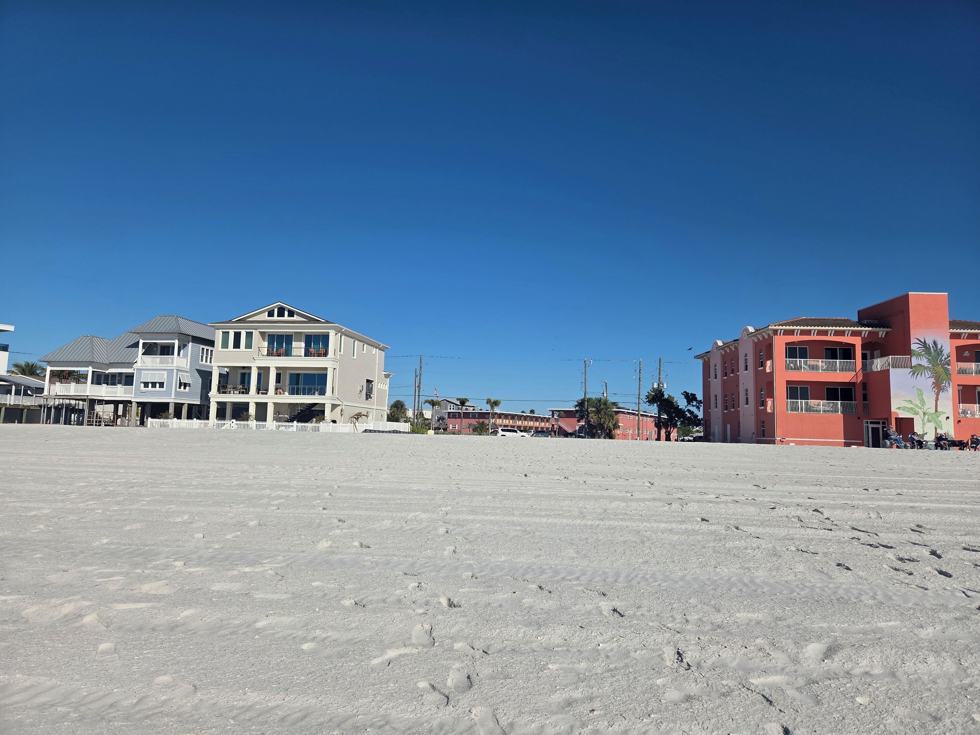 A beachfront property with a large sandy area, a multi-story building with balconies, and a smaller adjacent structure.