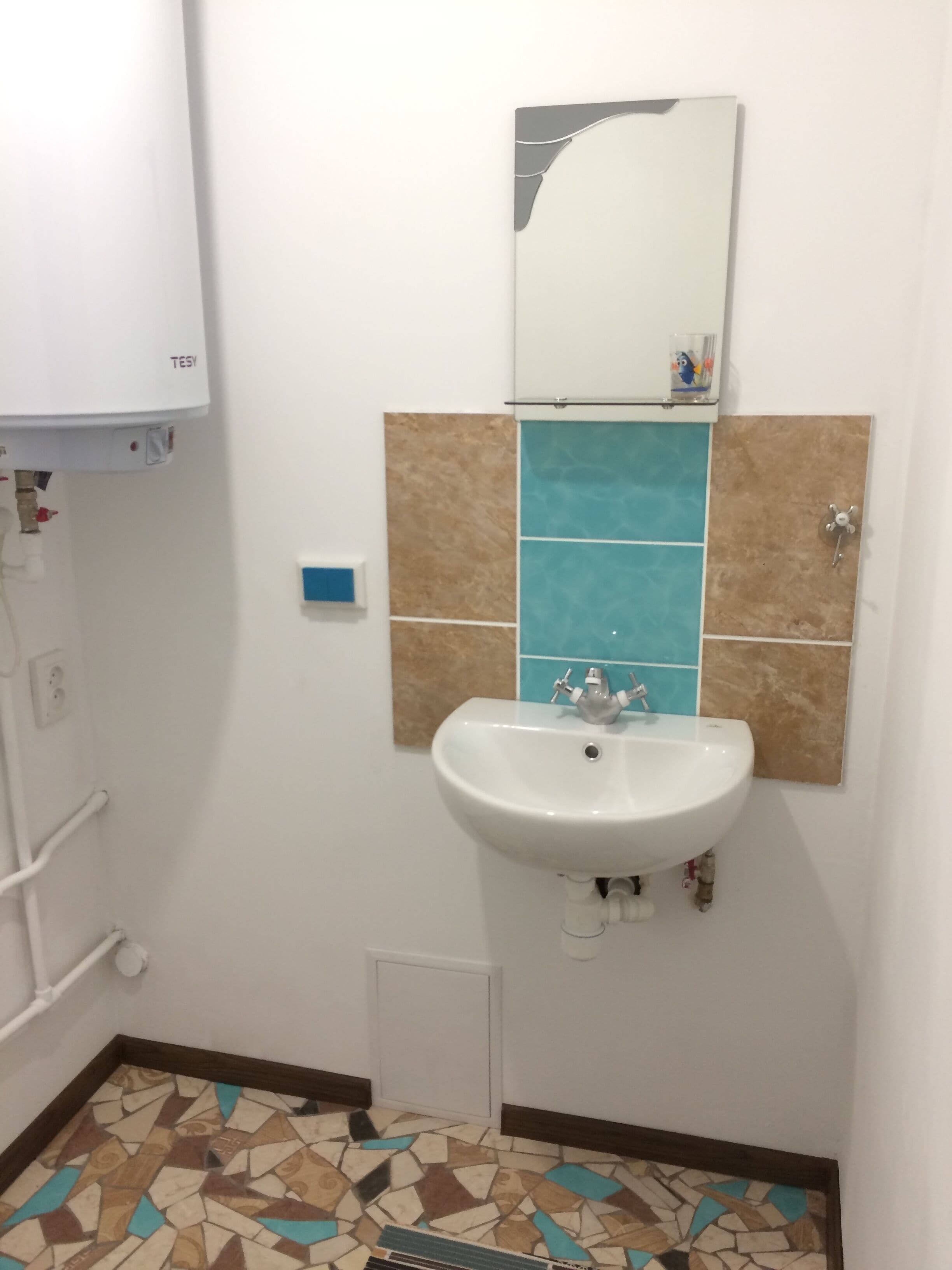 Een badkamer met een wit wastafel, een spiegel en een betegelde vloer.