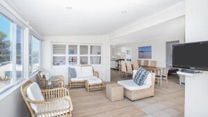 A spacious living area with wicker furniture, a dining table, and a flat-screen TV. - Mollymook At The Beach (Mollymook Beach)