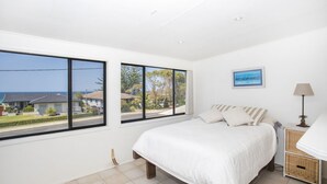 A bedroom with a large bed, two windows, a bedside table, a lamp, and a framed picture on the wall. - Mollymook At The Beach (Mollymook Beach)