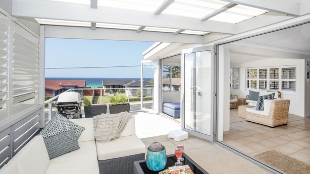 A modern living room with a sofa, a coffee table, and a view of the sea through large glass doors. - Mollymook At The Beach (Mollymook Beach)