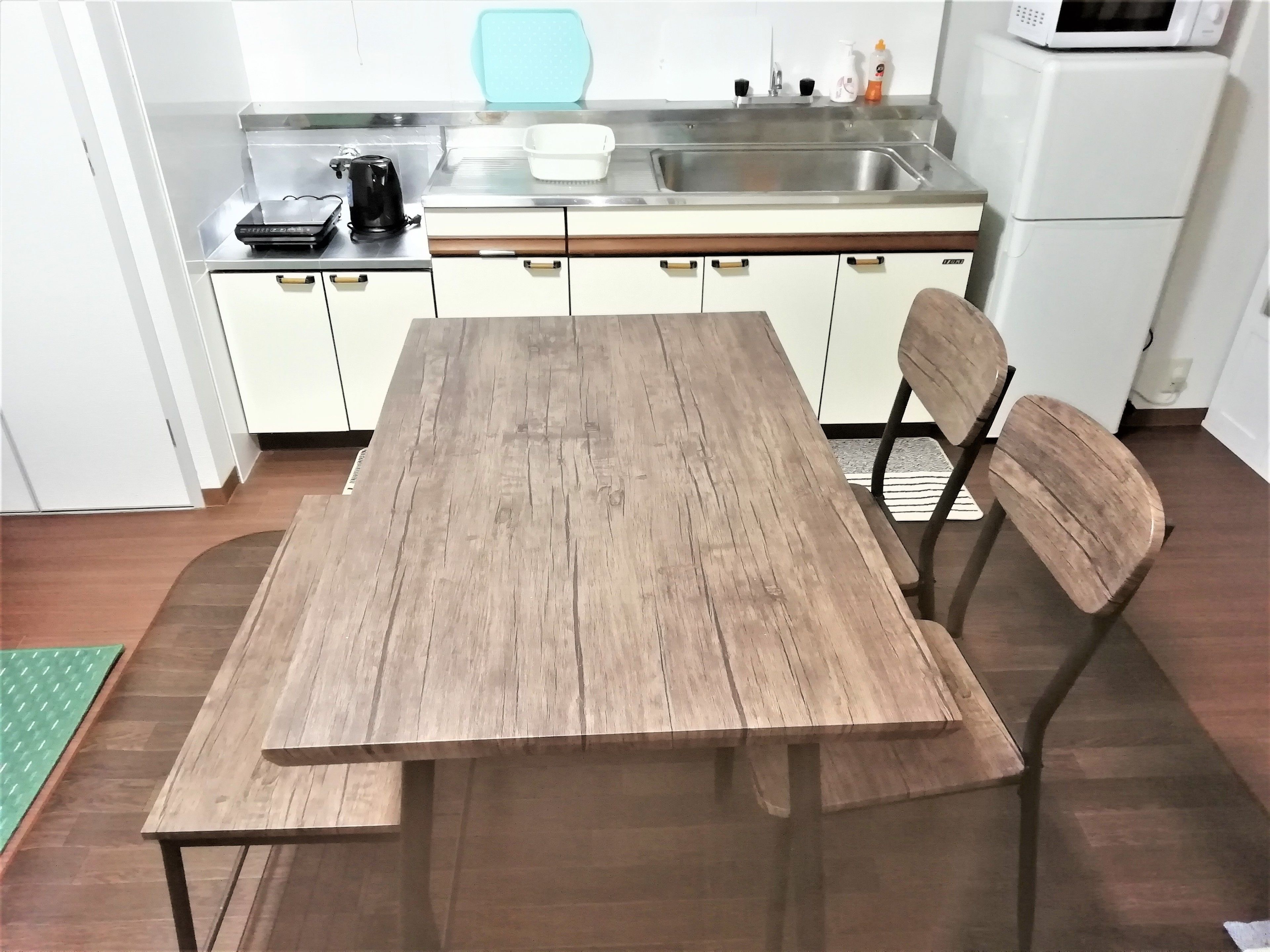 A kitchen with a wooden table, white cabinets, a microwave, and a kettle.