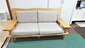 A wooden sofa with grey cushions in a room with white cabinets and a green patterned rug. - Apartment near Tram in Okayama (Okayama)