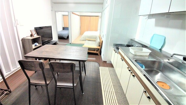 A compact hotel room with a kitchenette, a dining area with a table and chairs, a bed, and a television. - Apartment near Tram in Okayama (Okayama)