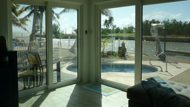 A room with a large sliding glass door leading to a pool area with a view of the water and palm trees. - Cozy Home!!!! (Marathon)