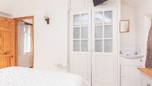 Une chambre à coucher avec un lit, une armoire blanche, un miroir et une salle de bain avec un lavabo.