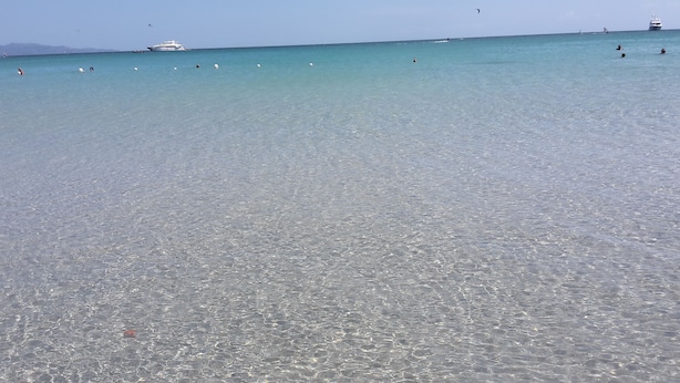Une plage propre avec une eau calme, des bateaux et des gens qui se baignent.