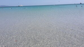 Ein sauberer Strand mit ruhigem Wasser, Booten und badenden Menschen.