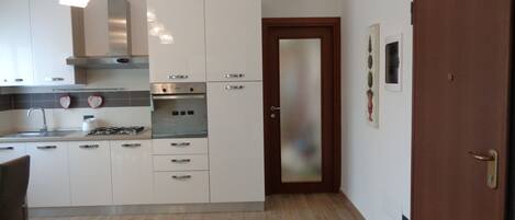 A modern kitchen with white cabinets, stainless steel appliances, and a wooden door.