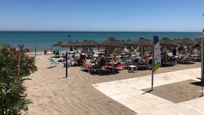 Un hôtel situé en bord de mer, doté de chaises longues, de parasols et offrant une vue dégagée sur l’océan.