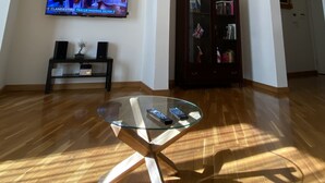 Ein geräumiges Wohnzimmer mit einem an der Wand befestigten Flachbildfernseher, einem Glastisch, Holzboden und einer dunklen Holzkommode.