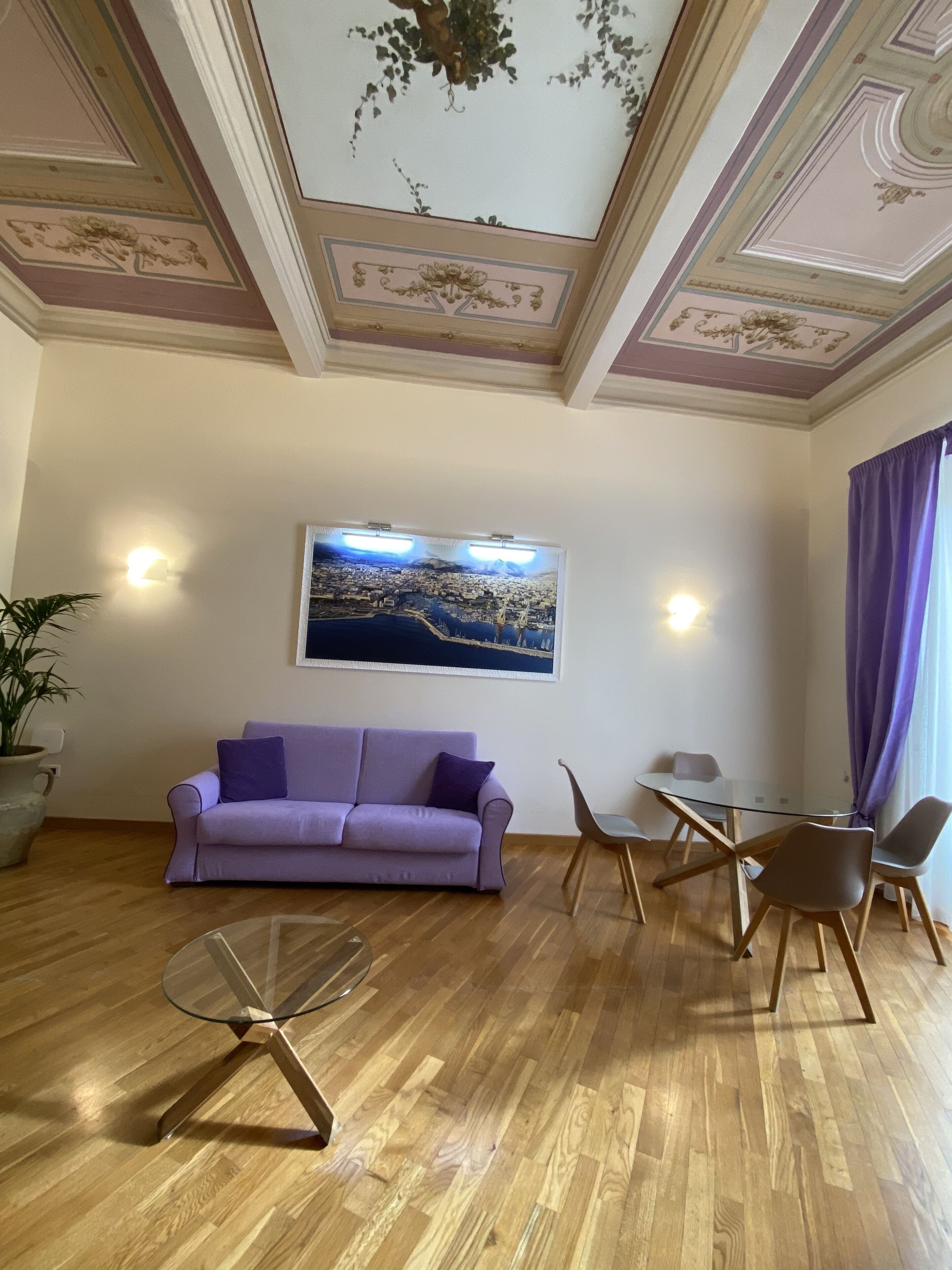 Ein Zimmer mit einem violetten Sofa, einem Glastisch und einer Essecke mit Stühlen.