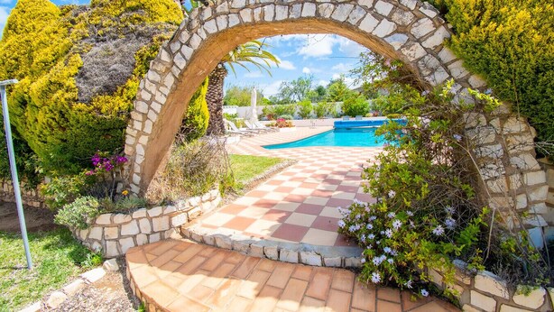 A stone archway leading to a pool area with a checkered pathway. - Casa Alegria · This villa is perfect for a family (Lagoa)