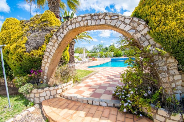 A stone archway leading to a pool area with a checkered pathway.